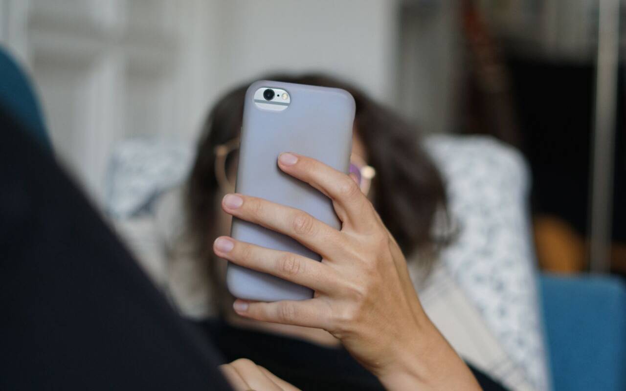 Eine Frau liegt auf einem Sofa und schaut sich ein Video auf der Social-Media-Plattform Instagram auf ihrem Handy an