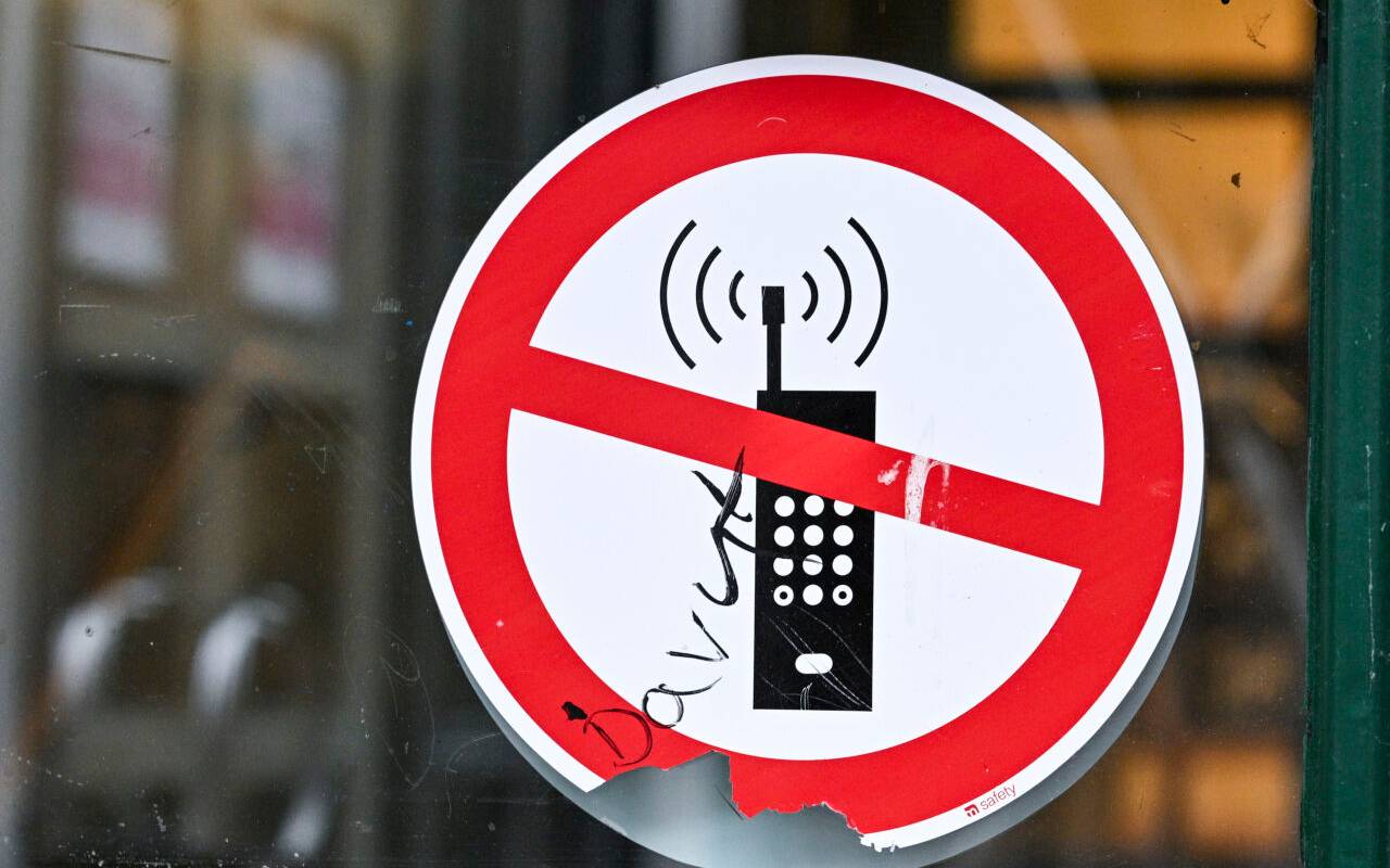 Ein Schild mit einem durchgestrichenen Handy-Symbol weist in einer Schule auf das Handyverbot hin.